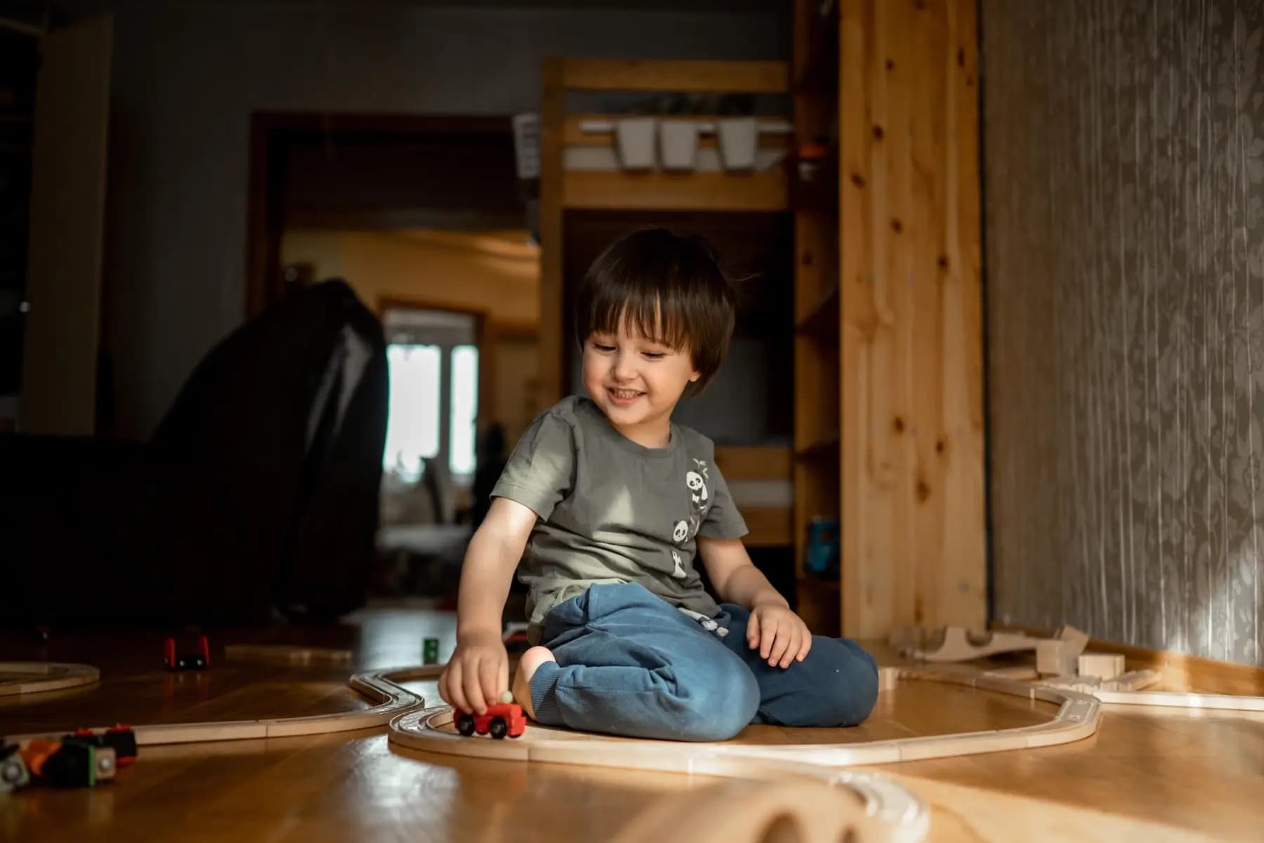 Kleiner Junge sitzt lachend auf dem Holzboden und spielt mit einer Holzeisenbahn