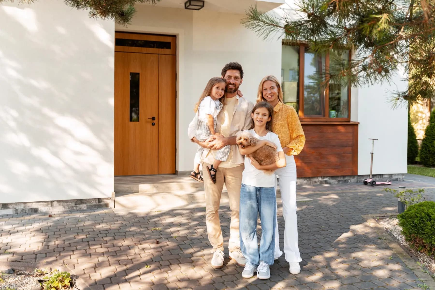 Familie mit zwei Töchtern und kleinem Hund steht vor einem modernen weißen Einfamilienhaus
